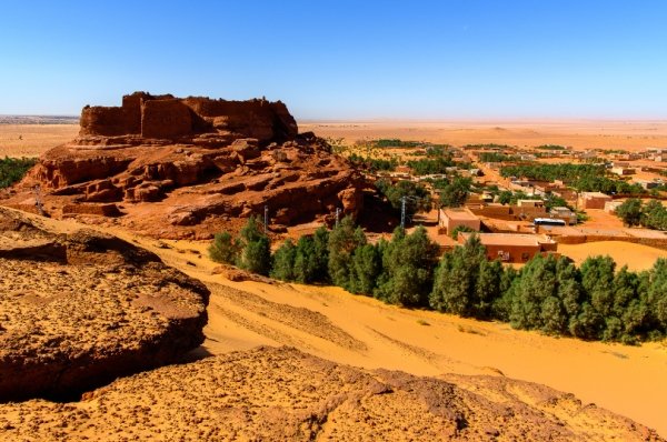 Paysage désertique ou se dresse les ruines d'une forteresse entour d'une palmeraie