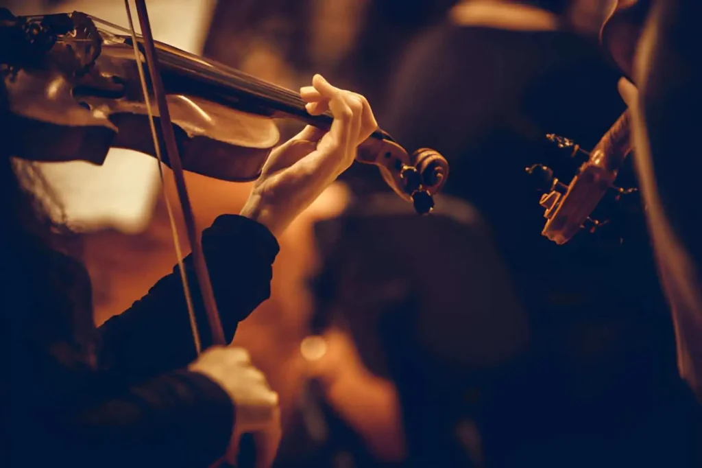 Photographie de l'Orchestre Symphonique de l'Opéra d'Alger sur la scène principale, musiciens en tenue de soirée avec violons et violoncelles sous des projecteurs dorés, architecture moderne de l'Opéra Boualem-Bessaïh en arrière-plan.