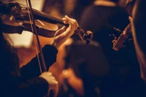 Photographie de l'Orchestre Symphonique de l'Opéra d'Alger sur la scène principale, musiciens en tenue de soirée avec violons et violoncelles sous des projecteurs dorés, architecture moderne de l'Opéra Boualem-Bessaïh en arrière-plan.