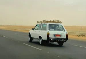 Illustration d'une Peugeot 504, exemple typique de voiture increvable d'occasion en Algérie, roulant au soleil couchant.