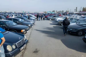 Vendeurs et acheteurs inspectant des voitures d'occasion, dont des Dacia Sandero et Renault Symbol, dans un marché en plein air. véhicule d'occasion en Algérie. marché véhicule occasion Algérie